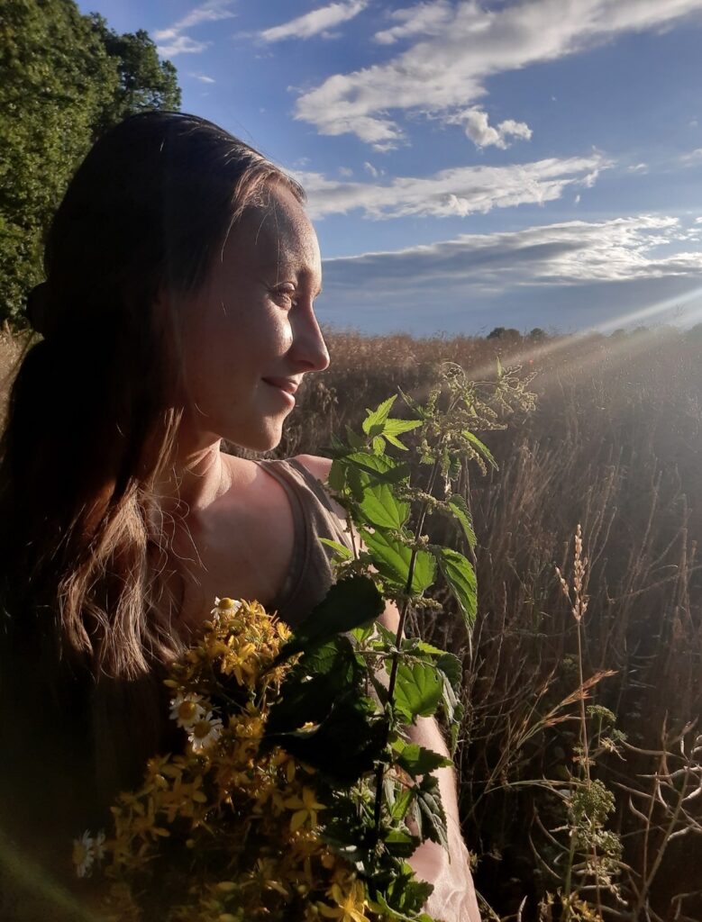 Frau Alessandra Moog mit Kräutern und Blumen am Waldrand.